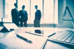 Business devices and documents at the workplace, unrecognized businesspeople sharing the ideas on the background